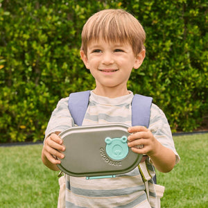 Child holding a GoodBare stainless steel snack box outdoors with greenery in the background