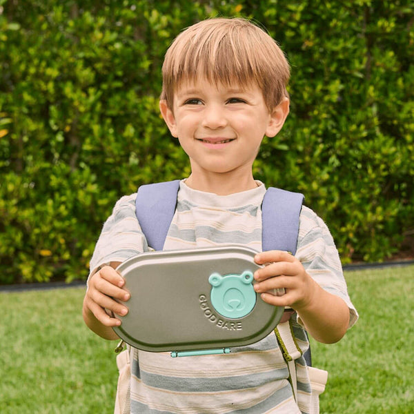 Child holding a GoodBare stainless steel snack box outdoors with greenery in the background