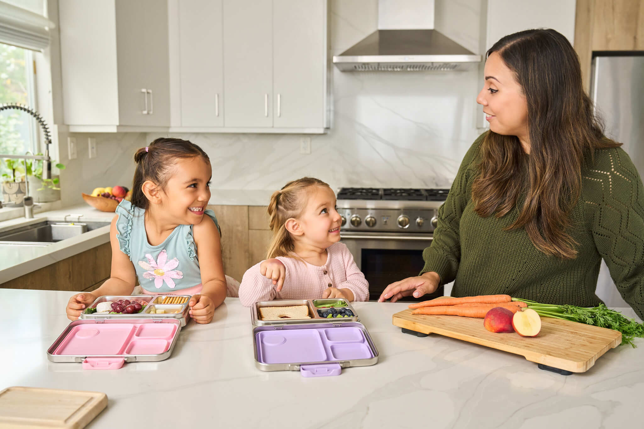 Mom and two children in a kitchen preparing food with leakproof stainless steel lunch boxes.